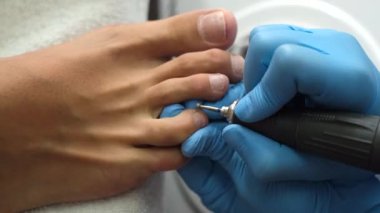 Pedikür süreci. Ev kuaförü pedikür. Ayak bakımı ve çivi. Profesyonel pedikür süreci işte. Mavi eldivenli usta manikür makinesiyle pedikür yapıyor..        