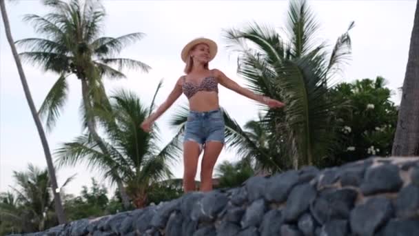 快乐的年轻欧洲女人 穿着豹纹比基尼 牛仔短裤 戴着经典的白色帽子 在热带奇异的海滩上 微笑着 摆出一副很开心的样子 玩乐的女孩度假 旅行的概念 — 图库视频影像