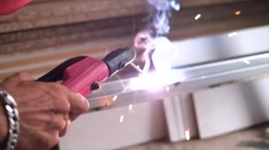 Fabrikada koruyucu maskeli bir işçi. Kaynak çelik profili. Bağlama yayı. Ateş, çalışmadan dolayı parıltı üretir