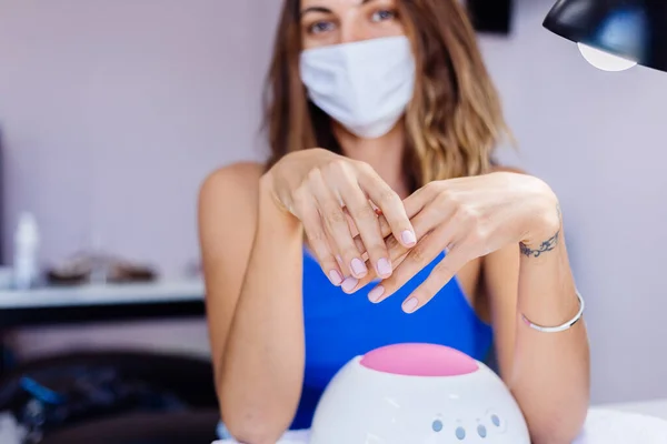 Woman in protective medical mask in beauty salon hold palette and select a color. Manicure procedure, nail care grand opening! Quarantine is over. Small businesses are open again.