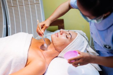 Yenilenme işlemi sırasında kozmetik uzmanının masasında yatan genç bir kadın. Kozmetik uzmanı boyun ve cilt bakımını genç ve sağlıklı bir şekilde üstlenir. Donanım yüz temizleme prosedürü.