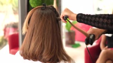Bir kız kuaför müşteriye keratin saç düzleştirici kullanarak düzleştirir. Kız siyah tıbbi maske takıyor. Sosyal mesafe. Koruyucu önlemler. Karantina sona erdi. 