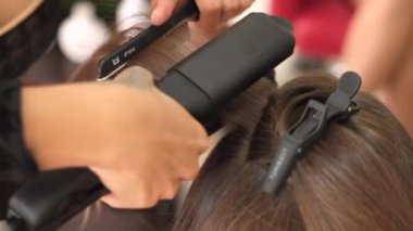 Bir kız kuaför müşteriye keratin saç düzleştirici kullanarak düzleştirir. Kız siyah tıbbi maske takıyor. Sosyal mesafe. Koruyucu önlemler. Karantina sona erdi. 