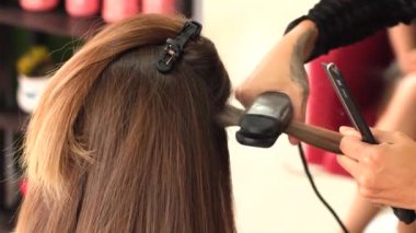 Bir kız kuaför müşteriye keratin saç düzleştirici kullanarak düzleştirir. Kız siyah tıbbi maske takıyor. Sosyal mesafe. Koruyucu önlemler. Karantina sona erdi. 