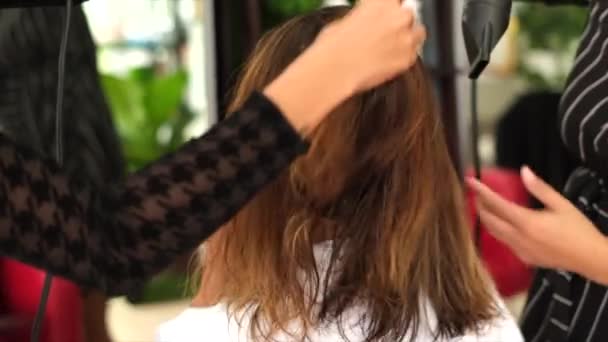 一个女理发师使客户的角蛋白头发直 这个女孩穿着黑色的医疗面罩坐在沙龙里 用吹风机吹风社会距离 保护措施 四只手 — 图库视频影像