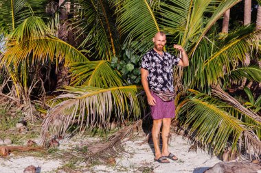  Bronzlaşmış, güzel görünümlü, beyaz kadın kot şortlu, yeşil modaya uygun hasat bluzlu, tropikal desenli pelerinli, gün batımında egzotik sahilde.  
