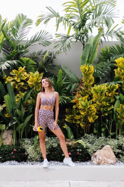 Moda stili, beyaz, formalı, spor, leopar desenli Cami tişörtlü ve motorcu şortlu bir kadın. Elinde protein karıştırıcı, bir şişe su var. Koşudan sonra suya susamış karın kaslı bir kadın.. 