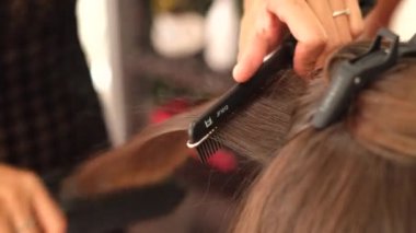 Bir kız kuaför müşteriye keratin saç düzleştirici kullanarak düzleştirir. Kız siyah tıbbi maske takıyor. Sosyal mesafe. Koruyucu önlemler. Karantina sona erdi..  