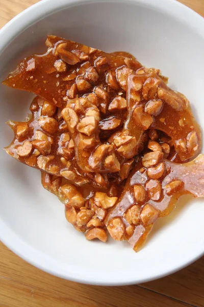 Peanut brittle pieces on a white bowl on wooden table