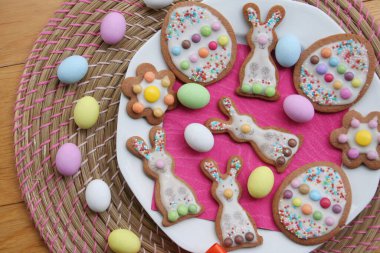 Tavşan şeklinde ev yapımı Paskalya kurabiyeleri ve tahta masada bir tabakta Paskalya yumurtası. İlkbahar arkaplanı