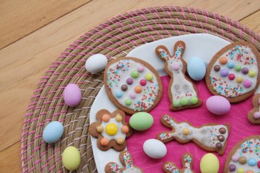 Tavşan şeklinde ev yapımı Paskalya kurabiyeleri ve tahta masada bir tabakta Paskalya yumurtası. İlkbahar arkaplanı