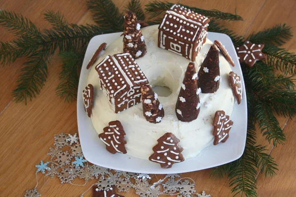 木製のテーブルの上に小さな家の形で装飾されたクッキーと白いチーズクリームで覆われたチョコレートケーキ — ストック写真