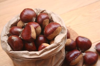 Kese kağıdındaki olgun kestaneler seçici odak üzerinde ahşap arka planda