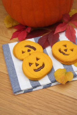 Balkabağı şeklinde cadılar bayramı kurabiyeleri. Tahta masada çikolata kremalı.