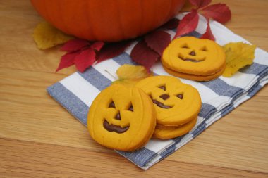 Balkabağı şeklinde cadılar bayramı kurabiyeleri. Tahta masada çikolata kremalı.