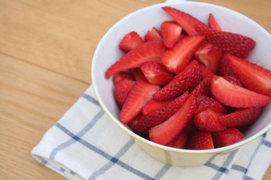 Tahta masadaki bir kasede parçalanmış taze olgun çilekler. Yaz meyveleri