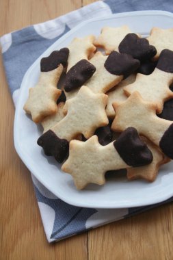 Tereyağlı kurabiyeler çikolatayla kaplanmış ve ahşap arka planda bir tabakta kayan yıldız şeklinde. Noel kurabiyeleri