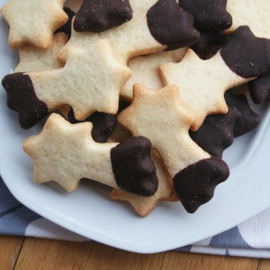 Tereyağlı kurabiyeler çikolatayla kaplanmış ve ahşap arka planda bir tabakta kayan yıldız şeklinde. Noel kurabiyeleri