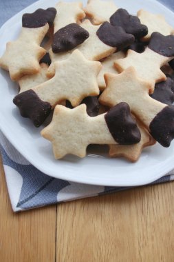 Tereyağlı kurabiyeler çikolatayla kaplanmış ve ahşap arka planda bir tabakta kayan yıldız şeklinde. Noel kurabiyeleri