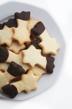 Beyaz arka planda izole bir tabakta kayan yıldız şeklinde çikolata kaplı tereyağlı kurabiyeler. Noel kurabiyeleri