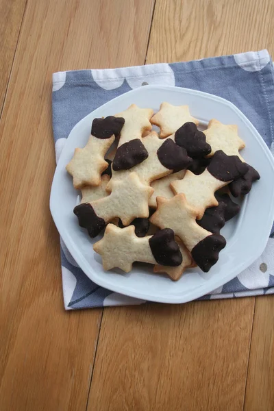 Tereyağlı kurabiyeler çikolatayla kaplanmış ve ahşap arka planda bir tabakta kayan yıldız şeklinde. Noel kurabiyeleri