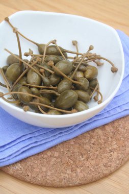 Tahta masadaki beyaz bir kasede yağlı kapari. İtalyan 