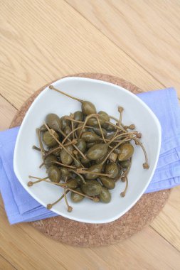 Tahta masadaki beyaz bir kasede yağlı kapari. İtalyan 
