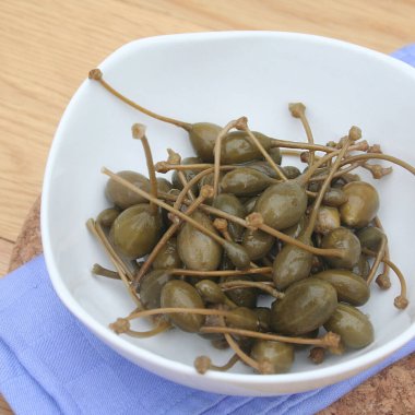 Tahta masadaki beyaz bir kasede yağlı kapari. İtalyan 