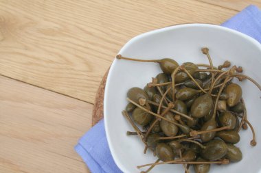 Tahta masadaki beyaz bir kasede yağlı kapari. İtalyan 