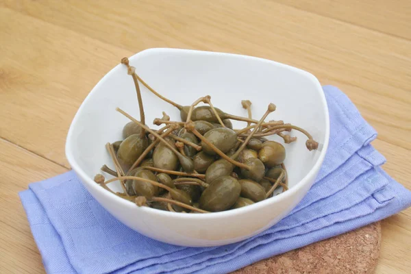 Tahta masadaki beyaz bir kasede yağlı kapari. İtalyan 