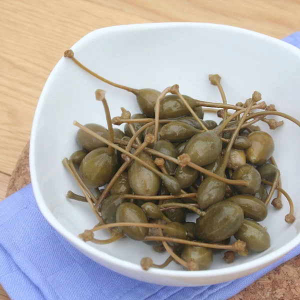 Tahta masadaki beyaz bir kasede yağlı kapari. İtalyan 