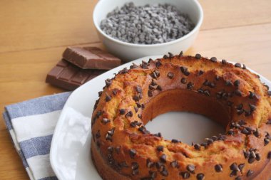 Yuvarlak tatlı pasta ve küçük siyah çikolata parçaları ahşap masada bir tabakta.