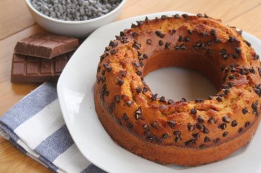 Yuvarlak tatlı pasta ve küçük siyah çikolata parçaları ahşap masada bir tabakta.