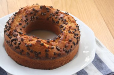 Yuvarlak tatlı pasta ve küçük siyah çikolata parçaları ahşap masada bir tabakta.