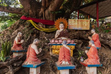 A vibrant, colorful Buddhist sculpture depicting Buddha with his followers is set at the sacred tree spot of Rangkut Monastery. The scene radiates spiritual significance, surrounded by natures tranquility and beauty.