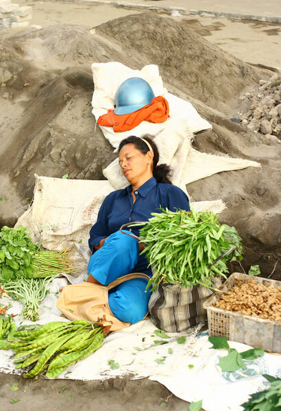 Yogyakarta, Indonesia - August 02, 2020: Fall asleep at work. A mother looks tired waiting for customers when she sells vegetables at the market. Indonesia is currently implementing the New Normal lifestyle.