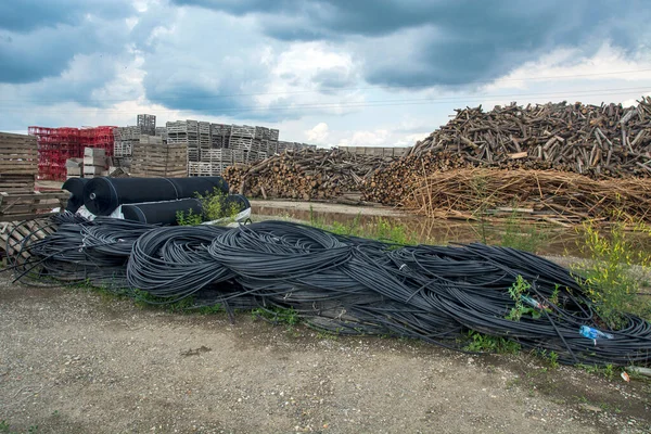 Huge hill of wood in storage. The logs are stored for processing in industry and stored in the open. There are also plastic decorated pipes as well as nets for crop protection in agriculture.