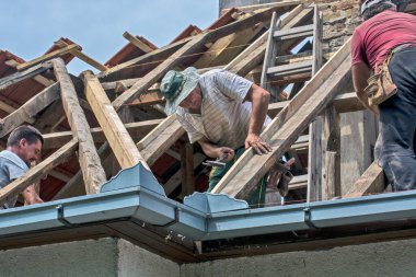 Zrenjanin, Sırbistan, 22 Temmuz 2020. Bir grup usta, eski bir fayans yerine özel bir evin çatısında çalışıyor. Güzel bir günü ve yağmursuz, istikrarlı bir havayı kullanıyorlar. Evin çatısından geçen çeşitli kablolar onları rahatsız ediyor..