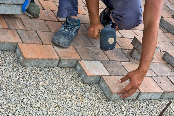 Master lay and install floor bricks on a public surface. The base is small stone and they fit concrete decorative pieces of brick.