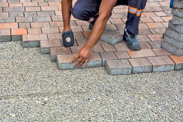 Master lay and install floor bricks on a public surface. The base is small stone and they fit concrete decorative pieces of brick.