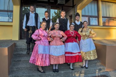 Ivanovo, Sırbistan, 15 Ağustos 2016. Folklor etkinliklerine katılan bir grup genç erkek ve kadın Kültür Evi önünde poz veriyor. Bulgar ulusal kostümleri giyiyorlar..