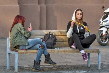 Zrenjanin, Sırbistan, 05 Ekim 2019. İki kız öğrenci, şehir merkezinde bir bankta dinleniyorlar. Güzel bir günün ve temiz havanın tadını çıkarırlar..