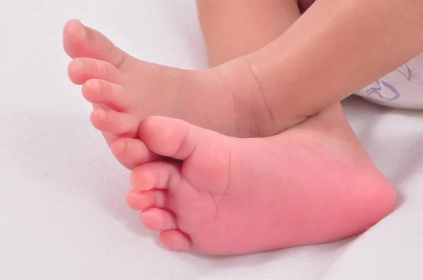 A little pinkish soft baby feet crossed over the other while sleeping in a white background.