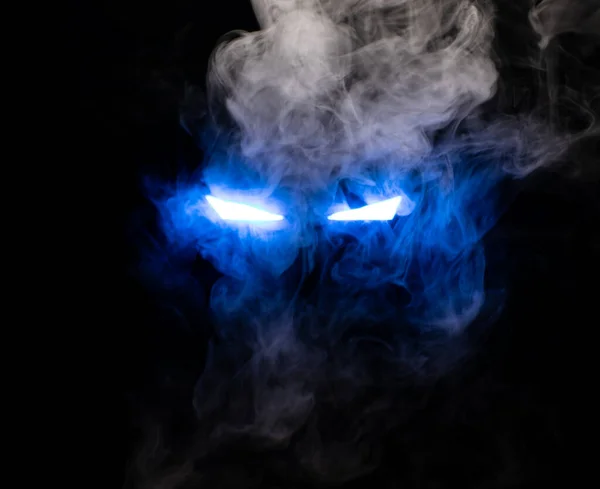 Ominous luminous eyes staring out of the darkness illuminate with rays of blue light swirling white smoke