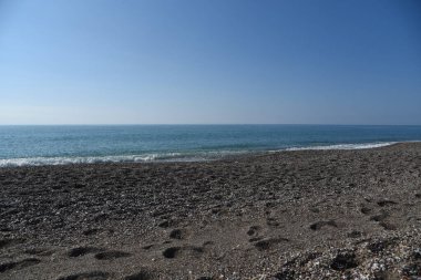 Mavi gökyüzünün arka planında ufukta sessiz dalgalar olan denizin su yüzeyi.