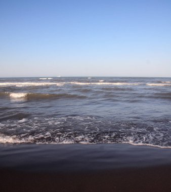 Mavi gökyüzünün arka planında ufukta sessiz dalgalar olan denizin su yüzeyi.