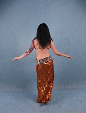 Altın etekli, oryantal elbiseli, stüdyoda duvağı olan, mavi arka planda güzel bir dansçı.