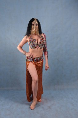 Altın etekli, oryantal elbiseli, stüdyoda duvağı olan, mavi arka planda güzel bir dansçı.