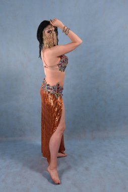 Altın etekli, oryantal elbiseli, stüdyoda duvağı olan, mavi arka planda güzel bir dansçı.