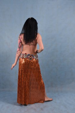 Altın etekli, oryantal elbiseli, stüdyoda duvağı olan, mavi arka planda güzel bir dansçı.